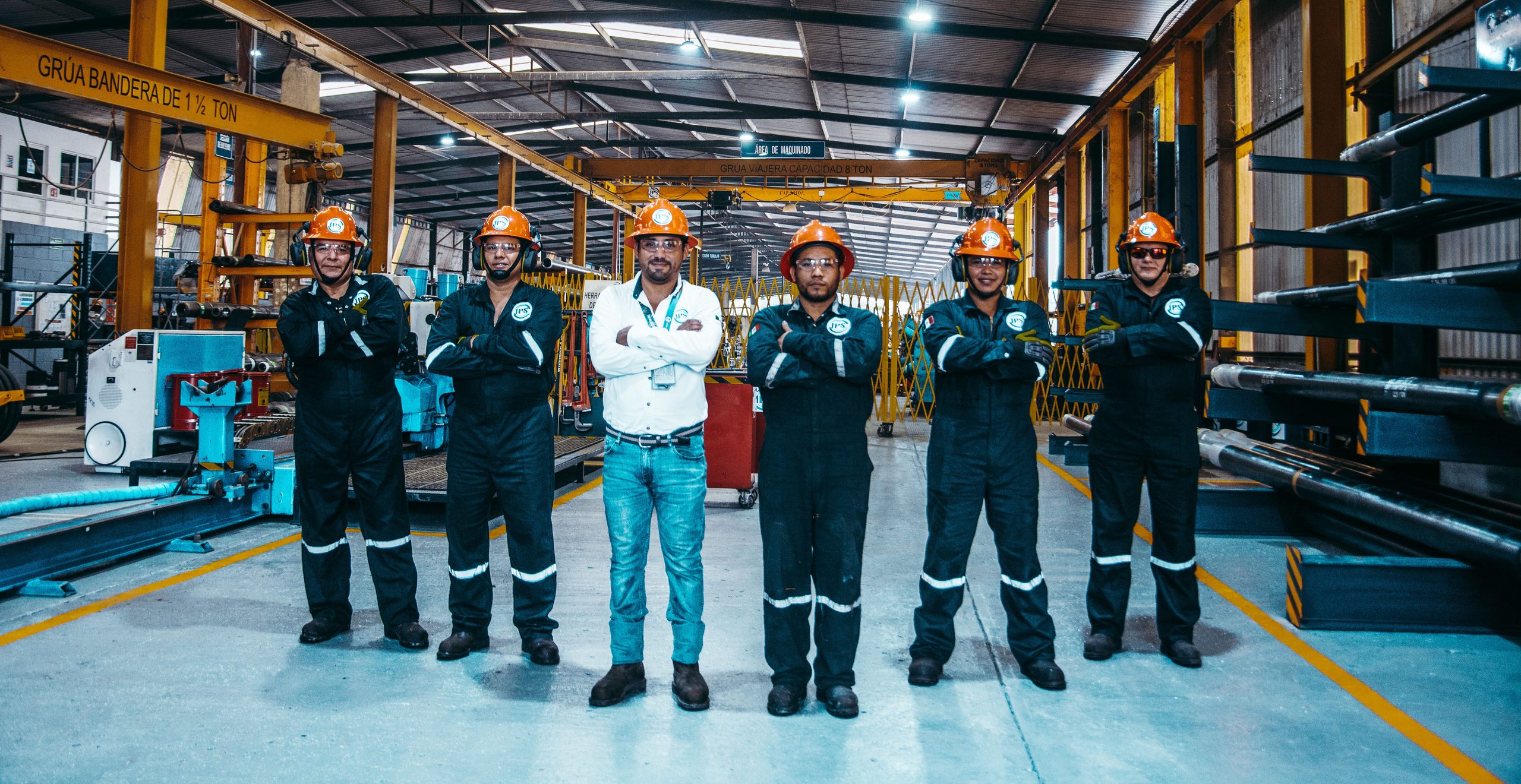 Six Grupo IPS team members standing with arms crossed on the workshop floor