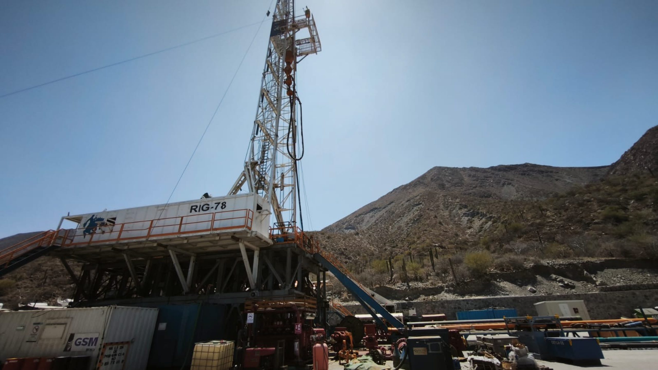 Drilling rig on a geothermal well pad below a rocky mountainside