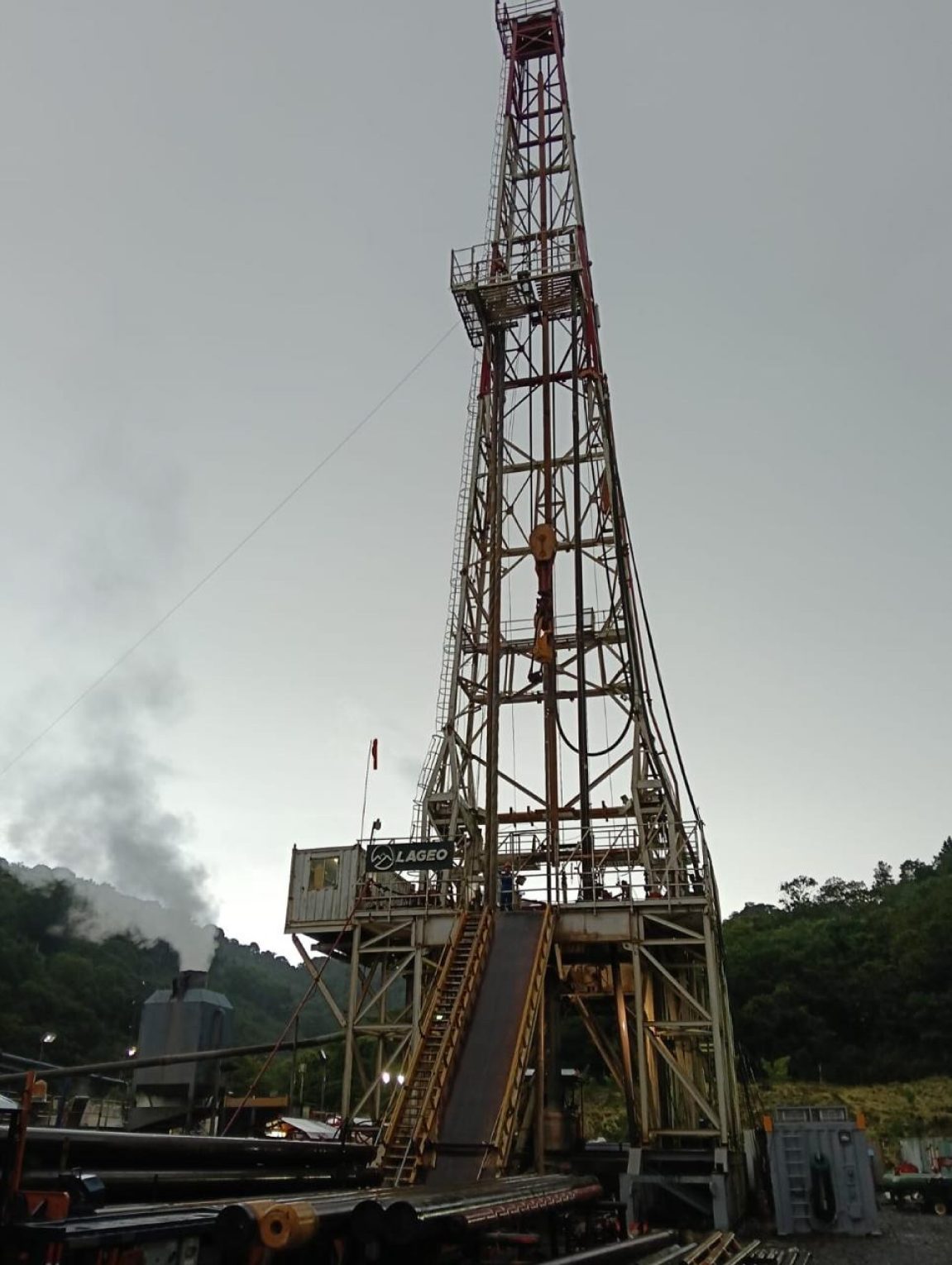 Drilling rig mast rising above a misty well site
